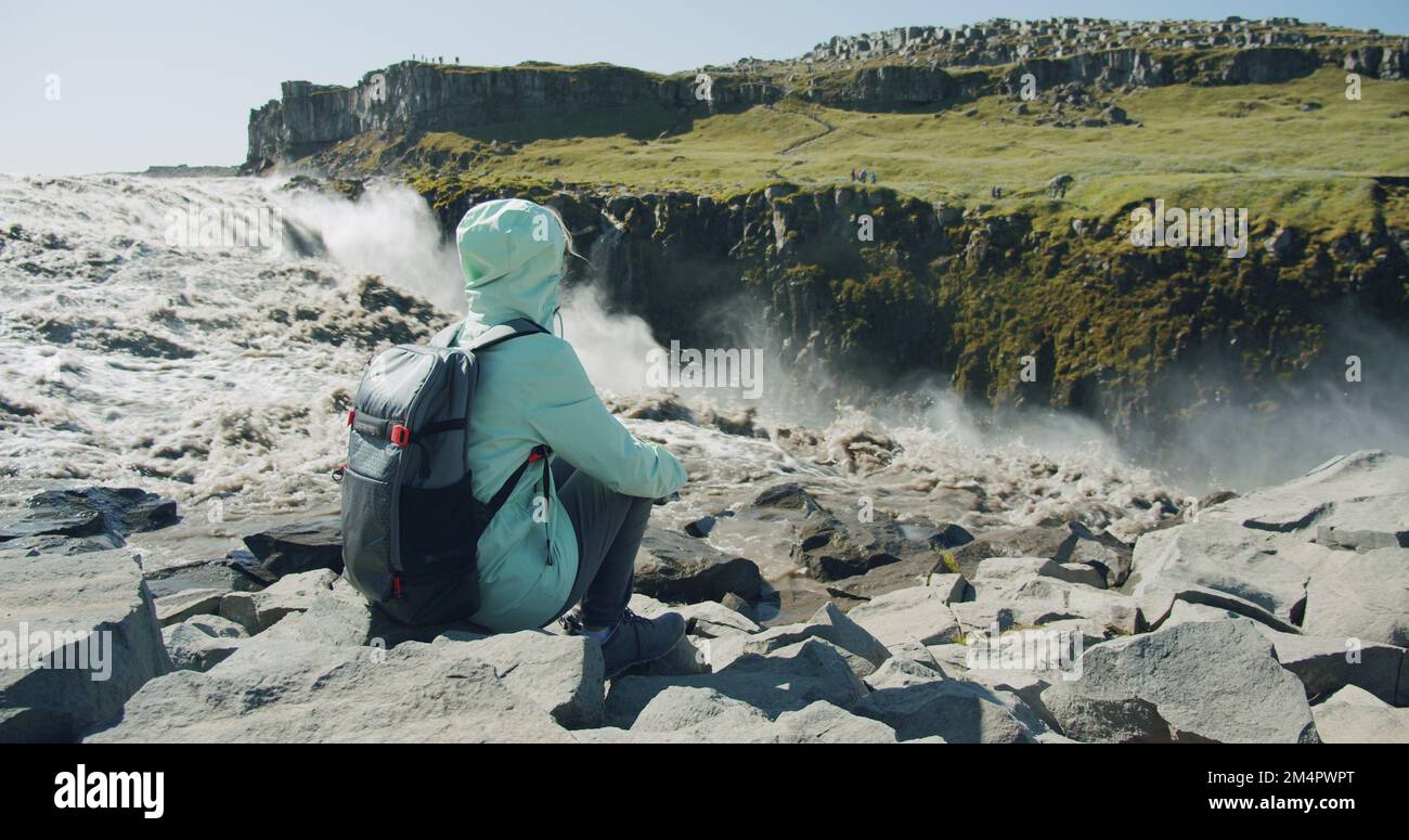Basalt Sitting Rocks Woman sitting on rocks enjoying powerful Detifoss waterfall and basalt ...