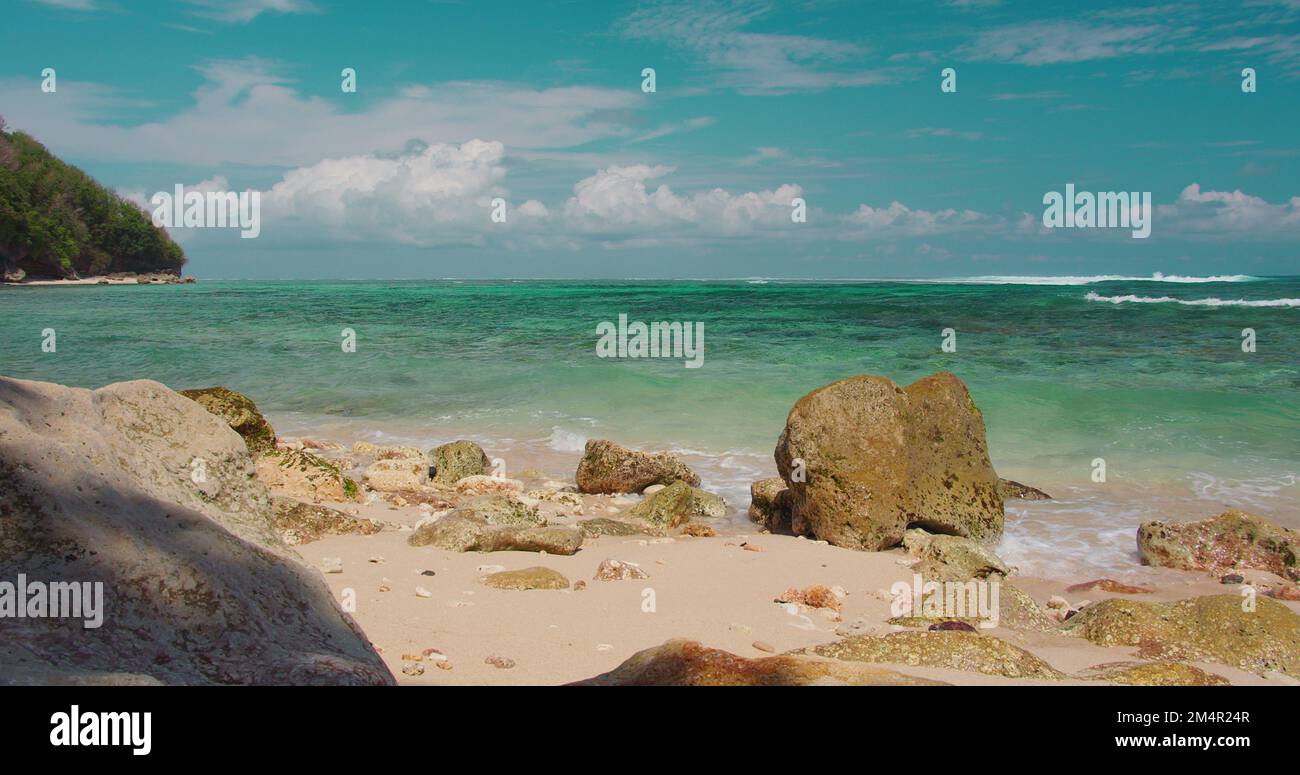 Tropical white sand beach sea water foams and spalshes on rocks, close ...