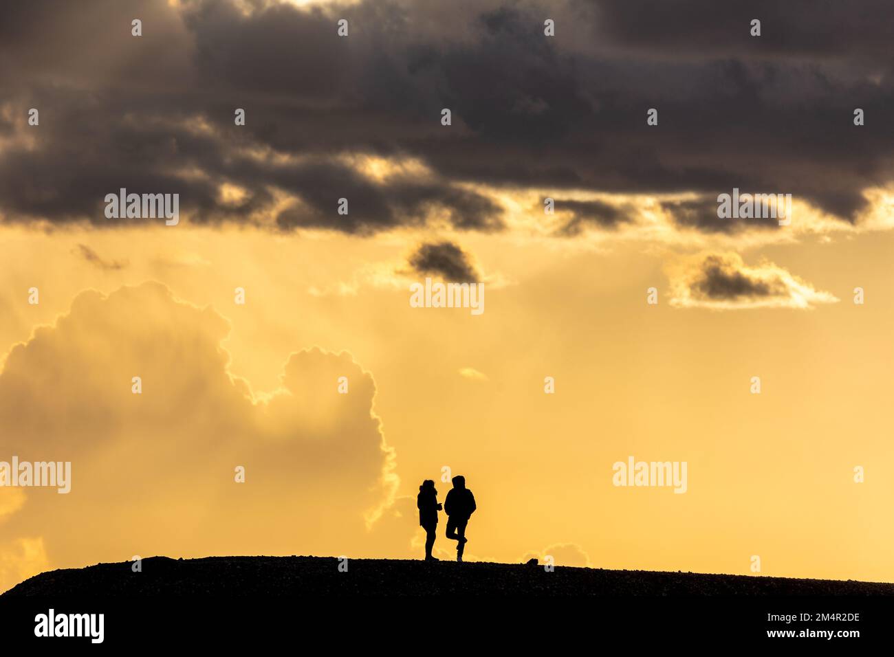 silhouette of a couple, woman and man, standing on a hill. Bright ...