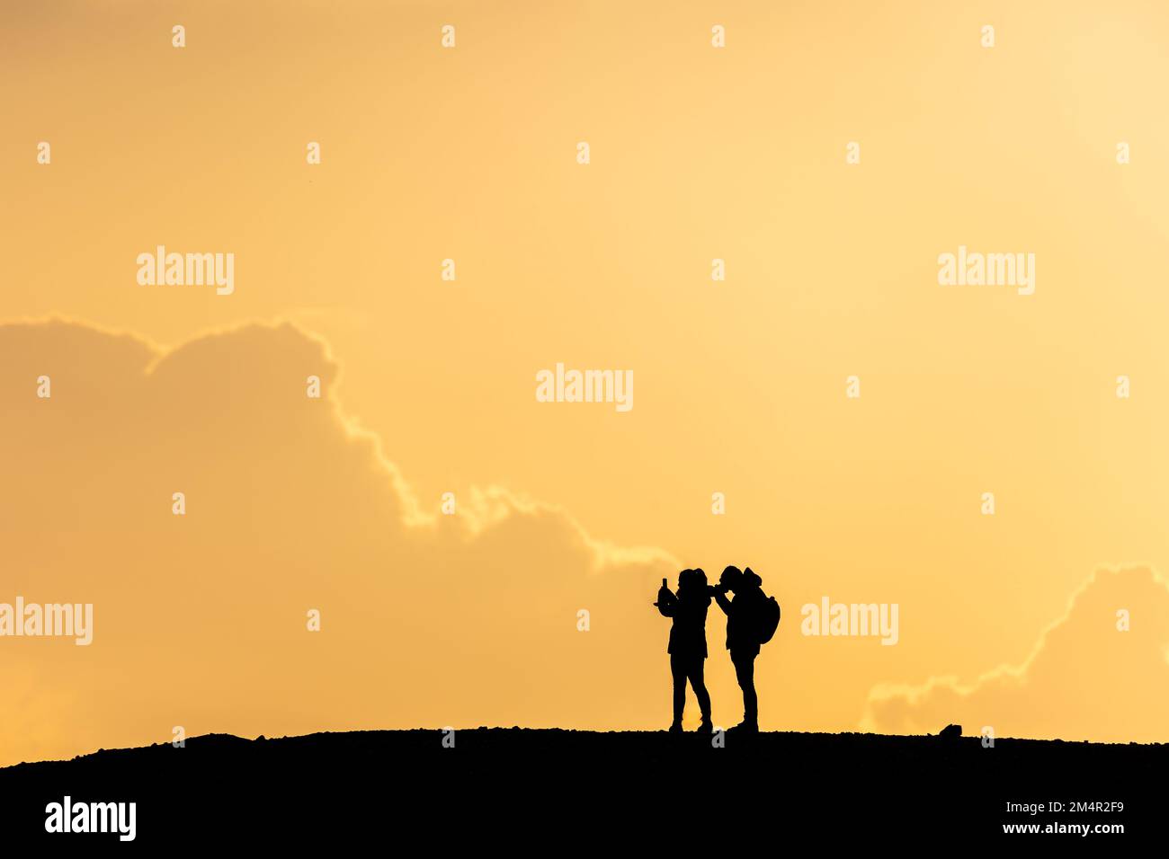 silhouette of a couple, woman and man, standing on a hill taking photos ...