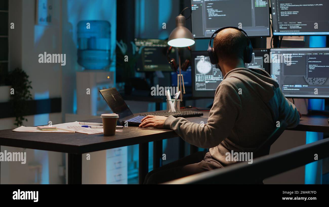 Software engineer typing programming code on laptop with multiple monitors, working with html script on terminal window. Developing algorithms and online cloud computing late at night. Stock Photo