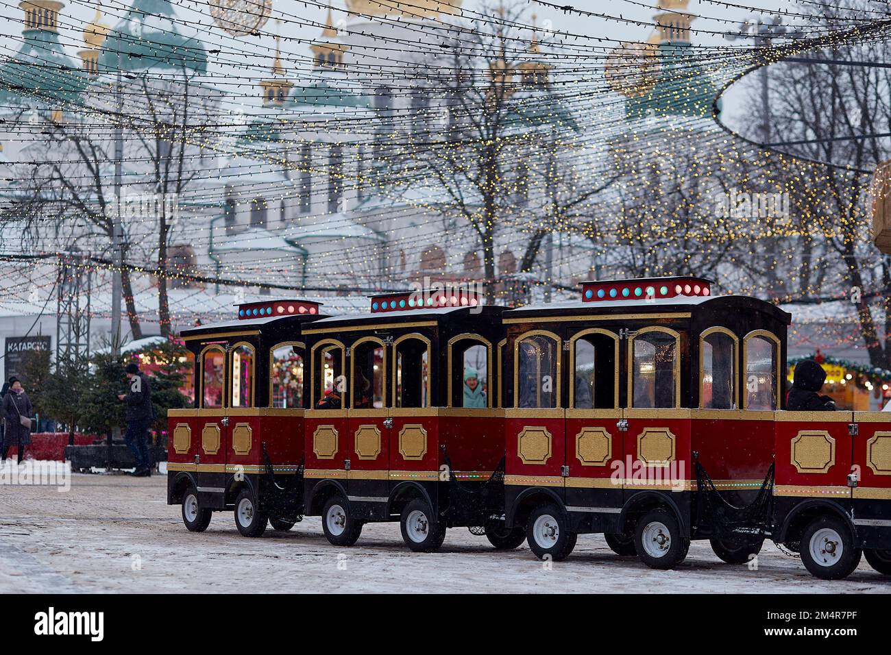 Kyiv, Ukraine - January, 2022: Joyful Christmas atmosphere with festive train in front of golden domes of the temple and lights at the evening. New Year holidays before war in Ukraine. Stock Photo