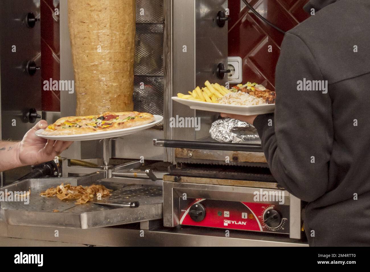 Employees of a kebab preparing typical kebab menu dishes with fries and rice and a frozen dough pizza Stock Photo
