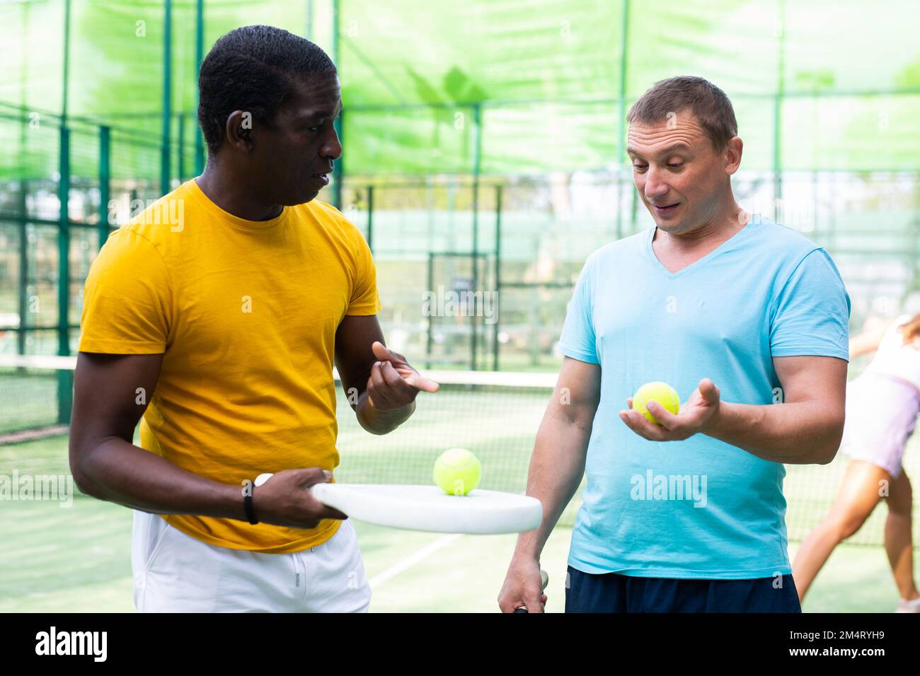 Two men with rackets in their hands chatting after playing padel on ...