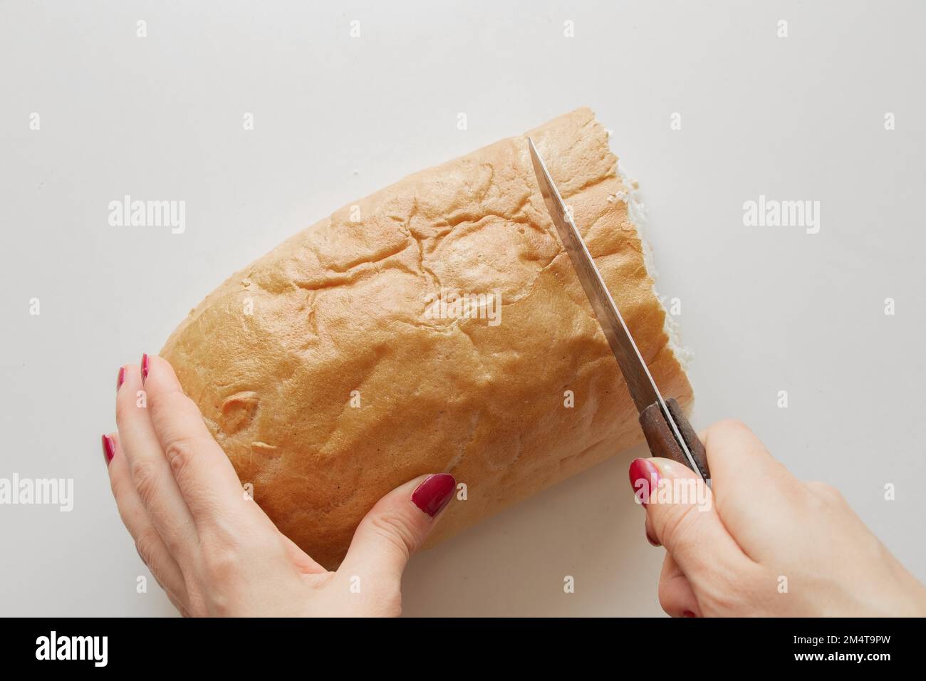 female hand cuts a piece of bread with a knife on a white table in the