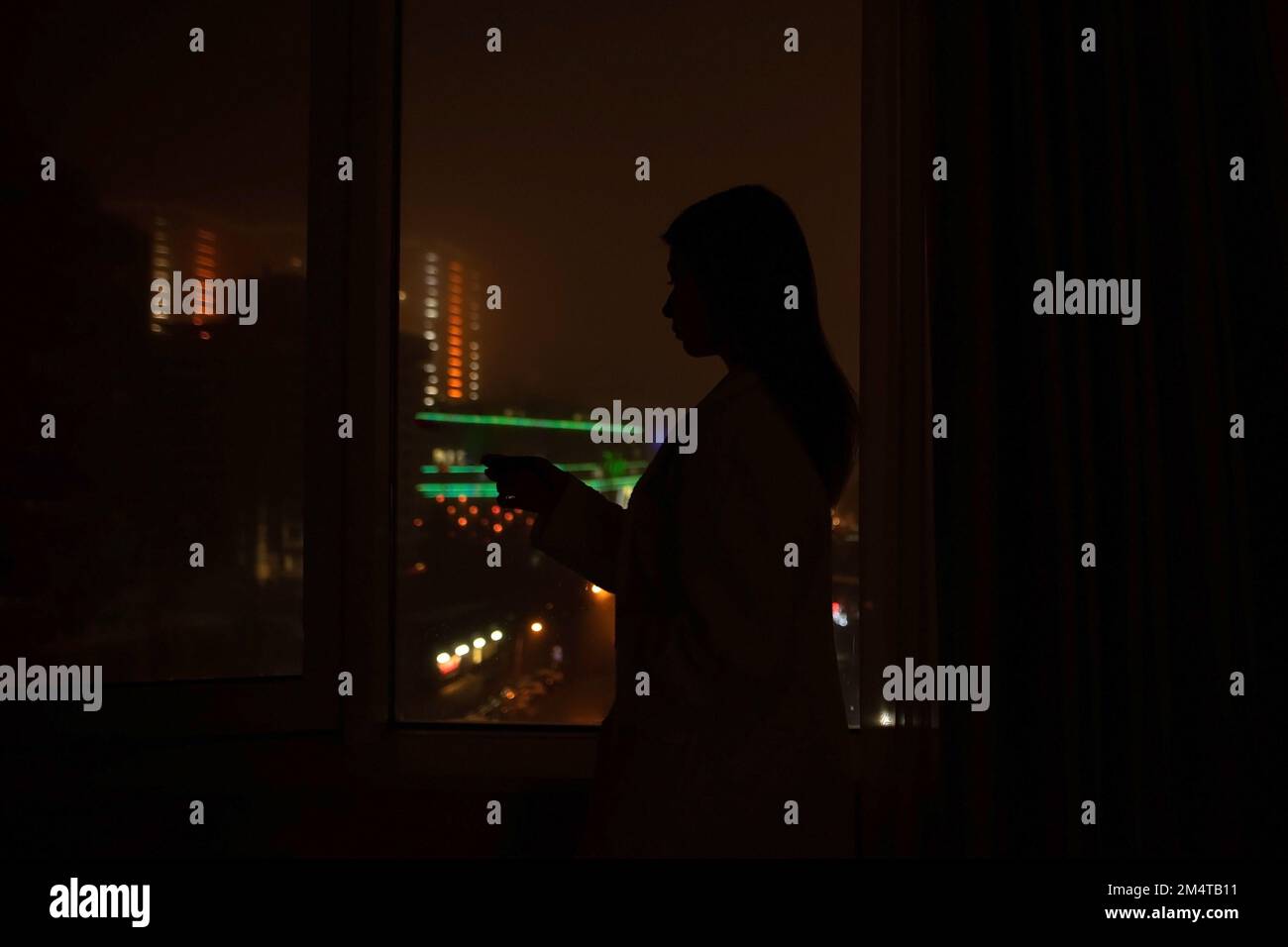 no light at home. woman silhouette near window in dark room watching