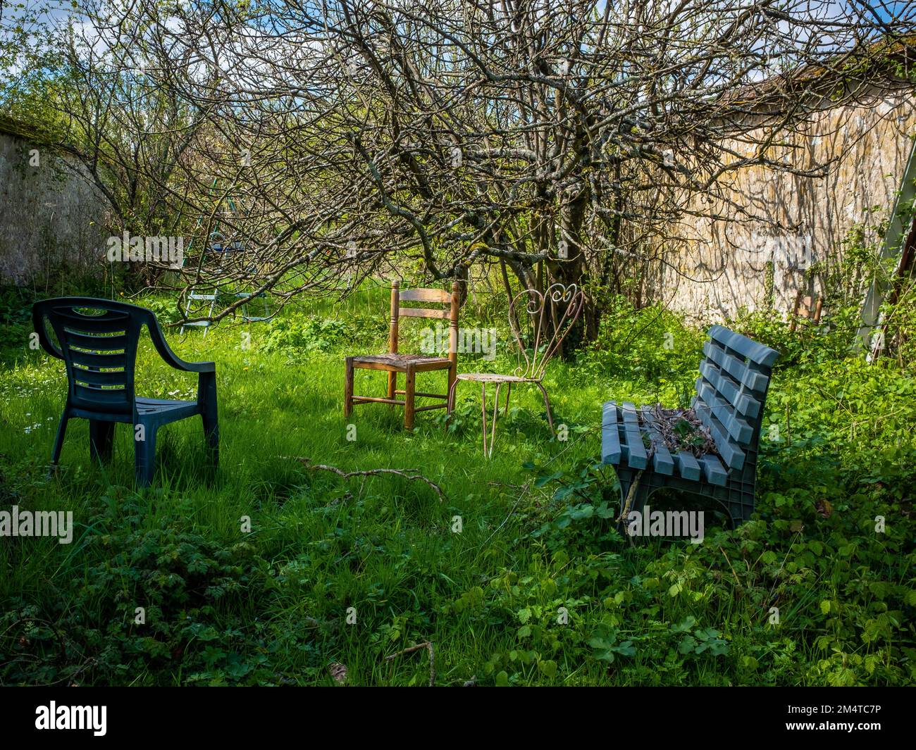 Abandoned chairs and a bench in an overgrown lawn closed with limestone walls, taken in the town of Thomery, near Paris on an early spring sunny day Stock Photo
