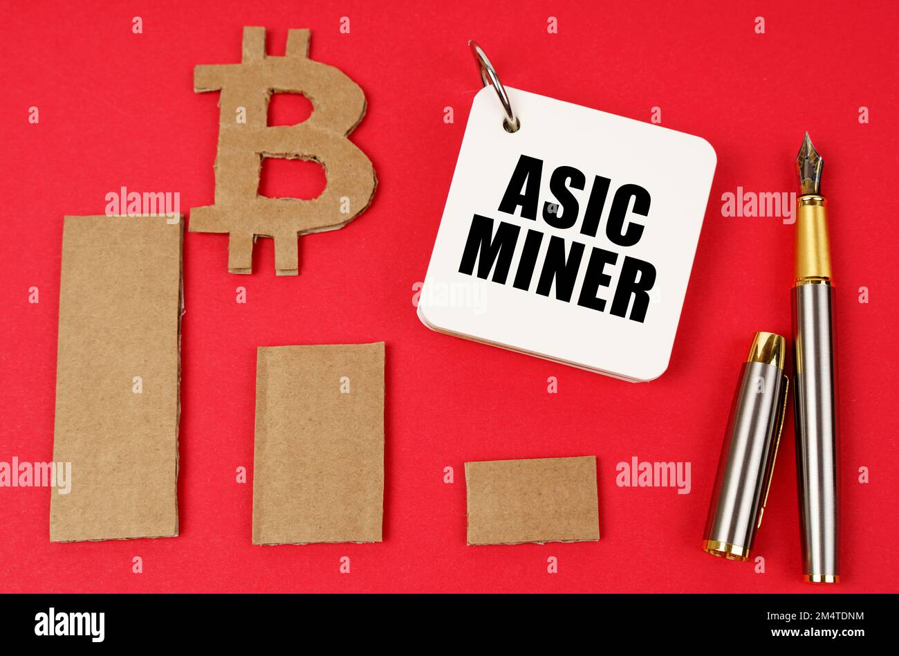 Business and bitcoin concept. On a red surface lie a bitcoin symbol, a graph, a pen and a notepad with the inscription - Asic miner Stock Photo