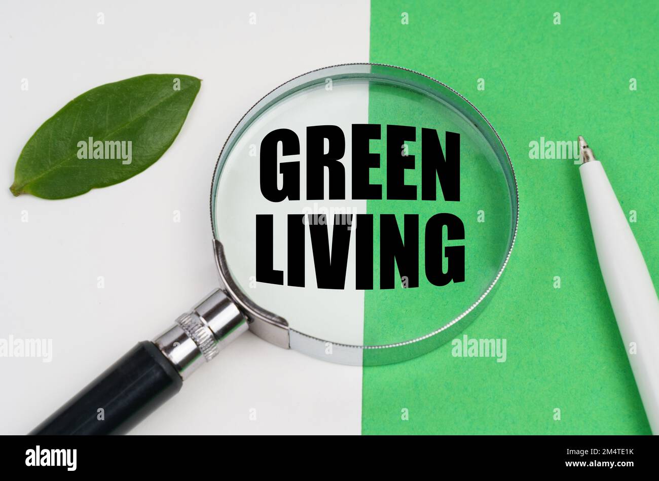 Ecological concept. On a white-green background lies a pen, a leaf of a plant and a magnifying glass, inside which is the inscription - Green Living Stock Photo