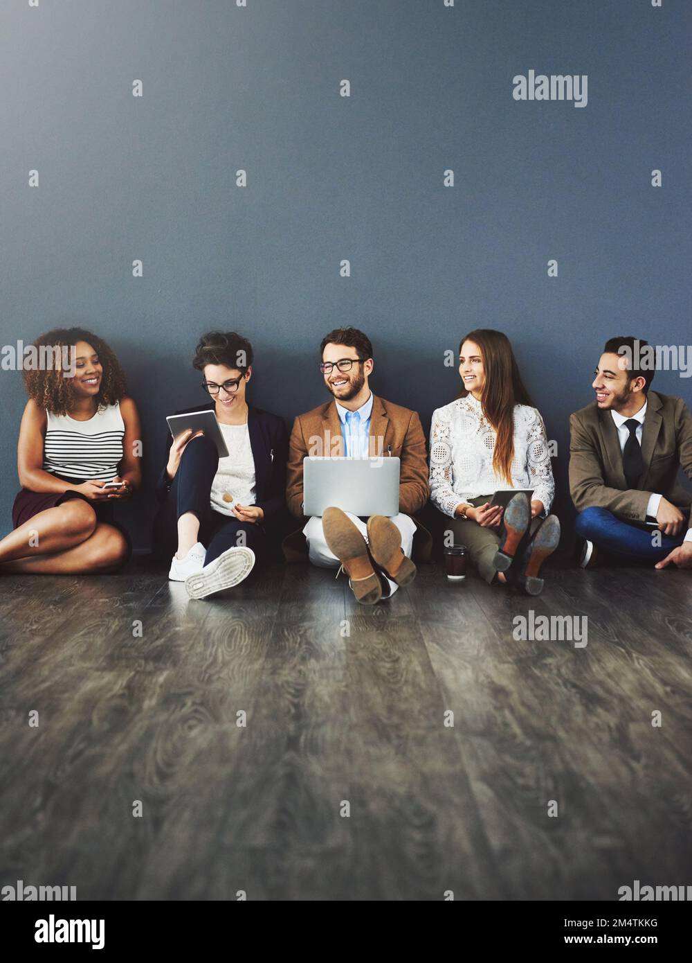 Connecting with the teammates. Studio shot of a group of businesspeople using wireless technology and talking on the floor against a gray background. Stock Photo