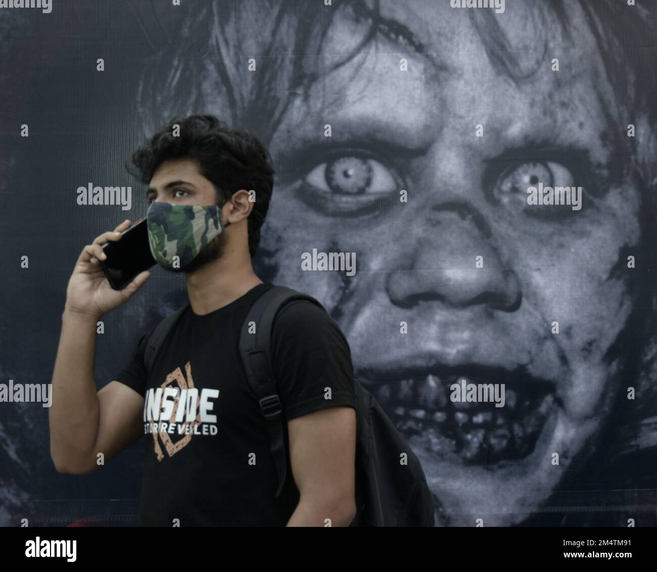 Man with a mask talking on phone infront of a scarry horror film poster. Unique, perfect timing photography. Stock Photo