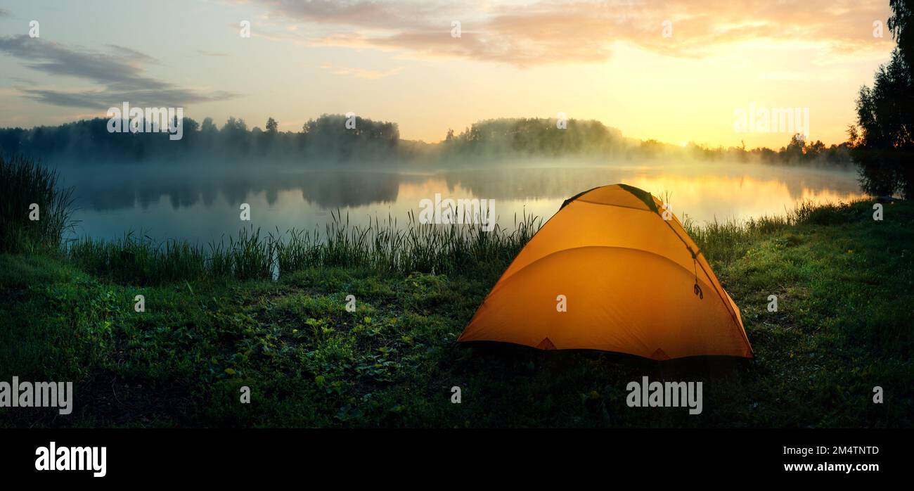 Orange tent on the bank of the river covered with fog in early morning Stock Photo