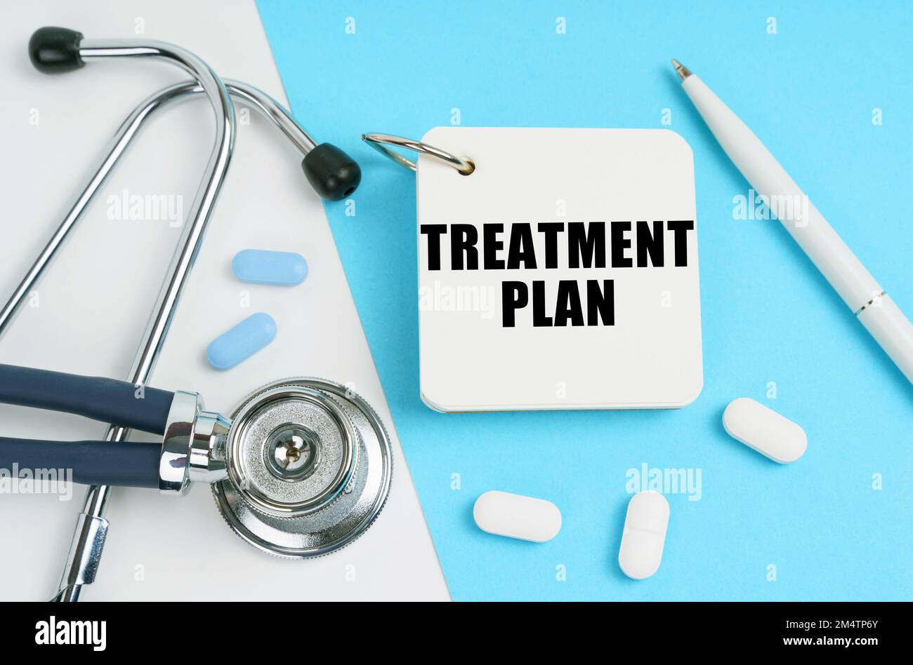 Medical concept. On a white and blue surface are pills, a stethoscope, a pen and a notepad with the inscription - TREATMENT PLAN Stock Photo