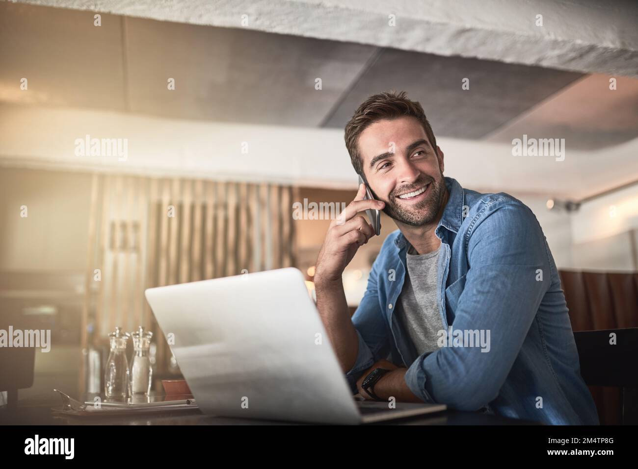 Who needs an office with a place like this. a handsome young man using a laptop and phone in a coffee shop. Stock Photo