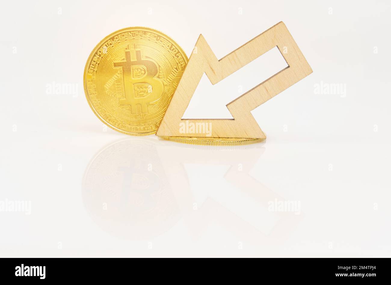 Cryptocurrency and business concept. On a white surface, bitcoin and an arrow showing a decrease in the value of the cryptocurrency. Stock Photo
