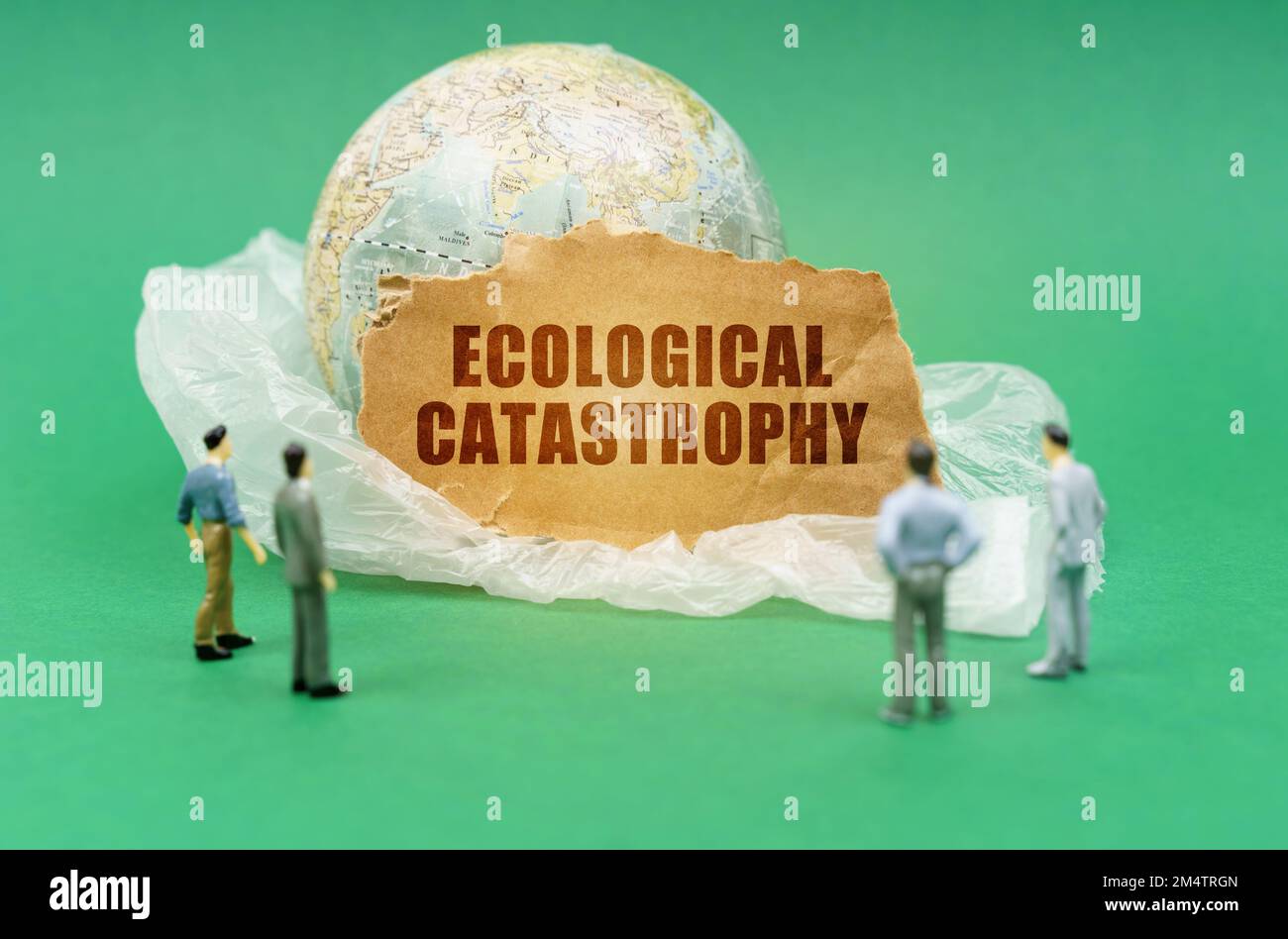 Ecological concept. On a green background on a plastic bag is a globe and a sign with the inscription - Ecological catastrophy. Near out of focus figu Stock Photo