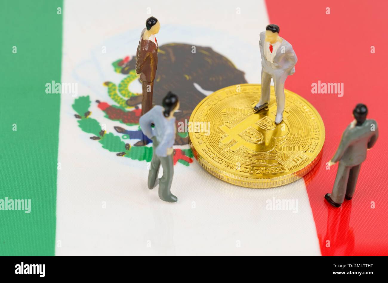 Cryptocurrency and business concept. On the surface with the image of the flag of Mexico are bitcoins and miniature figurines of people. Stock Photo