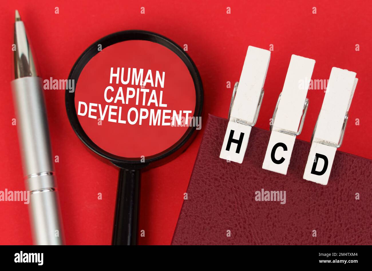 Business concept. On the red surface lies a pen, a notebook with clothespins - HCD, and a magnifying glass with the inscription - Human Capital Develo Stock Photo