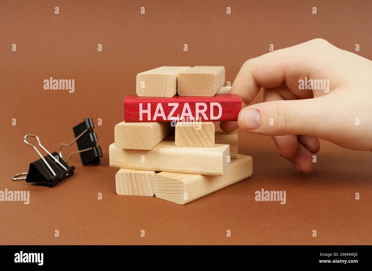 Industrial concept. Clamps and wooden blocks lie on a brown surface, a person takes out a red block with the inscription - danger Stock Photo