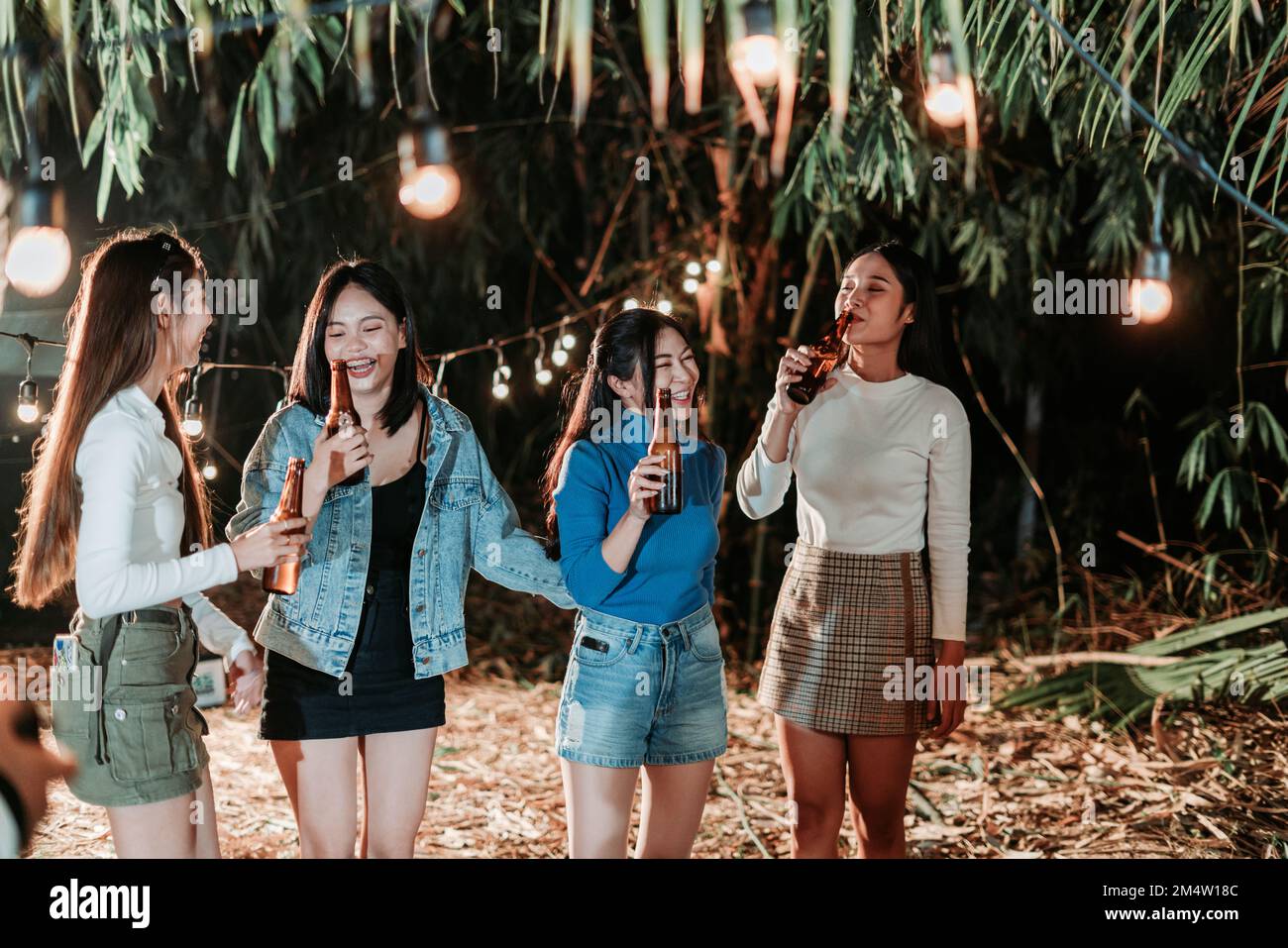 Group of female friends having fun holding bottles and drinking beer at the party Stock Photo