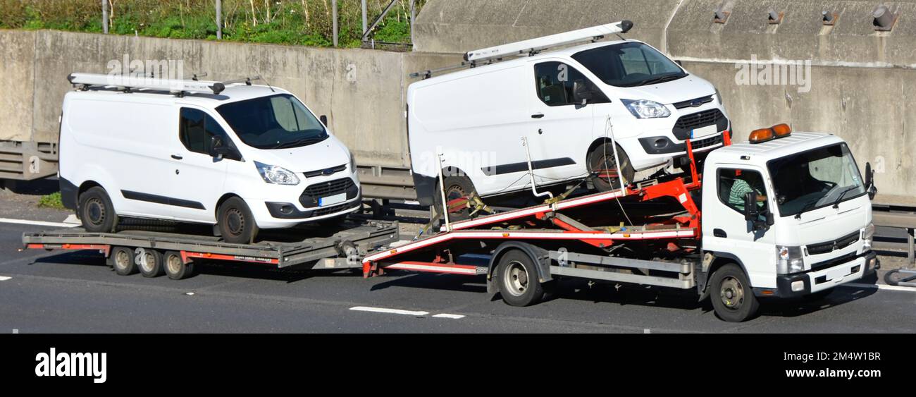 Ford white Transit van conveyed on commercial vehicle transporter & towing second Ford white Transit van loaded onto trailer driving on UK motorway Stock Photo