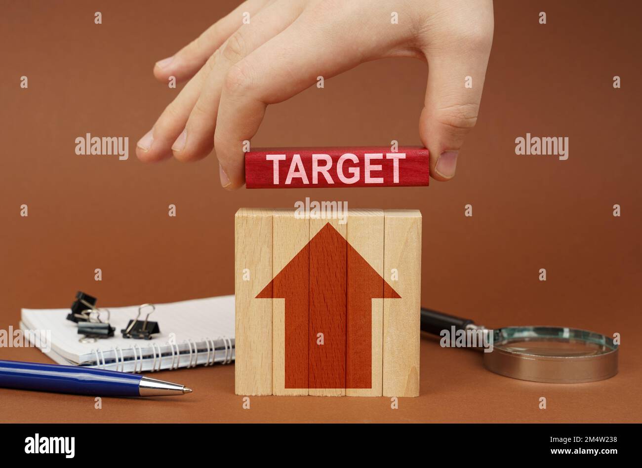 Business concept. On a brown surface are office items, wooden blocks, in the hand is a red block with the inscription - Target Stock Photo