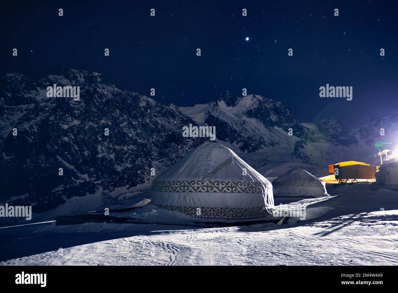 Yurt or yurta nomadic house at Ski resort Shymbulak in Almaty, Kazakhstan. Winter night astrophotography with stars against mountain peak Stock Photo