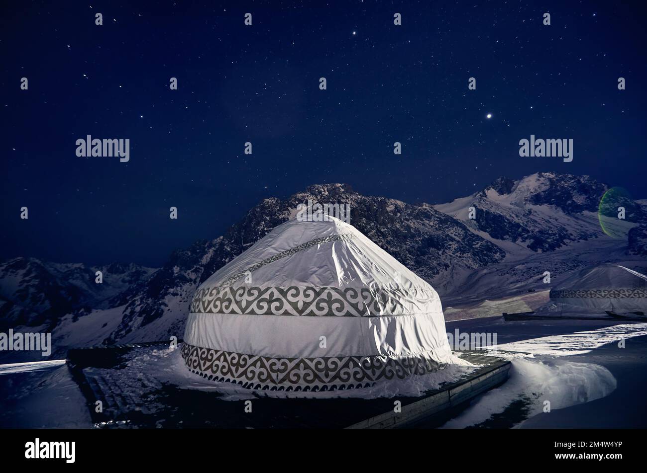 Yurt or yurta nomadic house at Ski resort Shymbulak in Almaty, Kazakhstan. Winter night astrophotography with stars against mountain peak Stock Photo