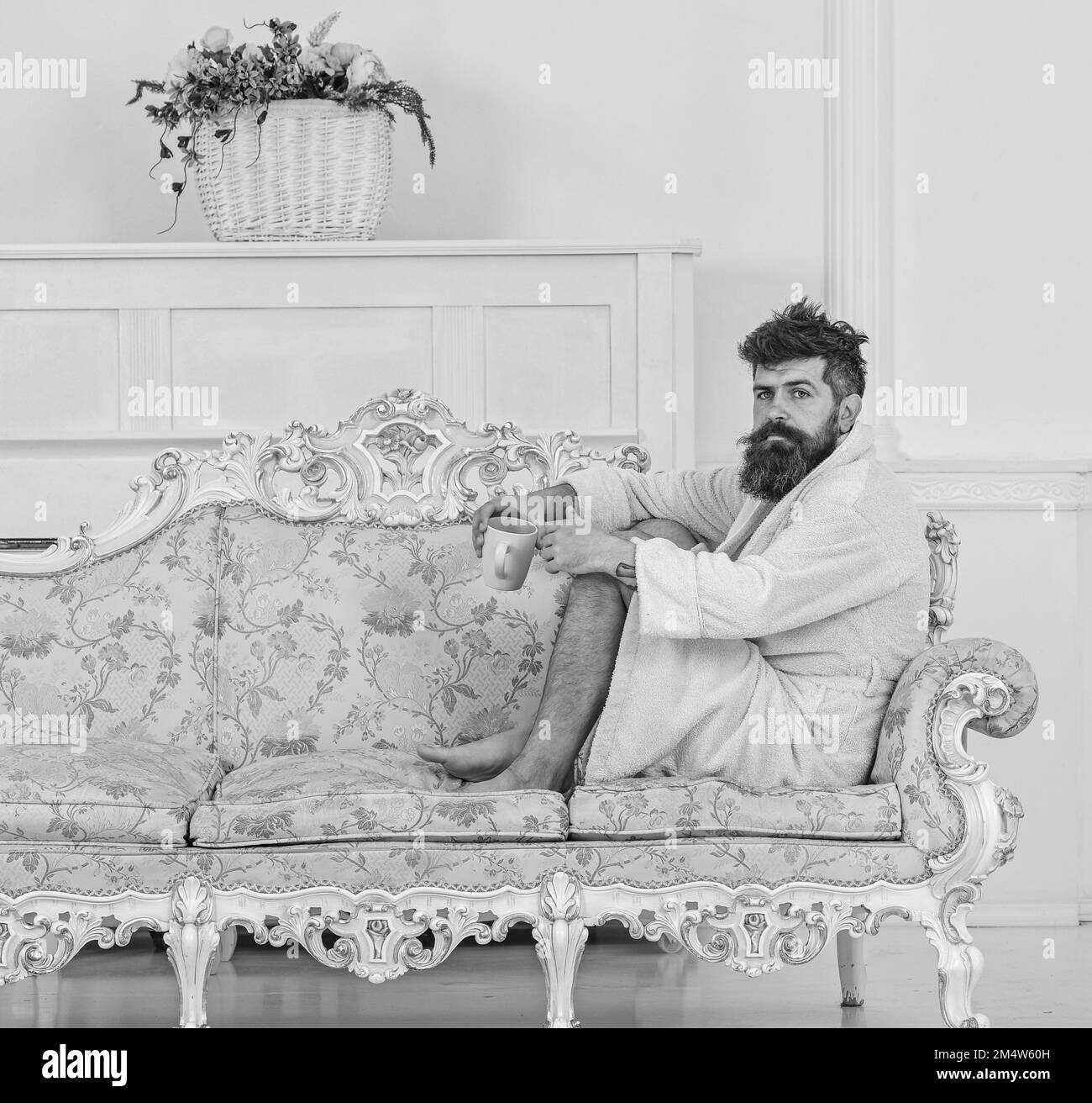 Man with beard and mustache enjoy morning while sitting on old fashioned luxury sofa. Luxury life concept. Man on thoughtful face in bathrobe drink Stock Photo