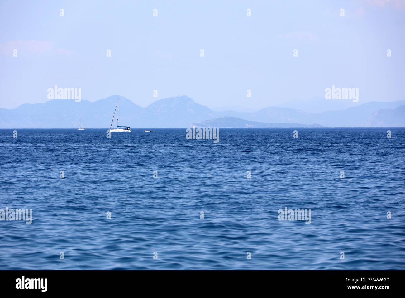 Picturesque view to blue sea with sailing yachts and mountain islands on horizon in mist. Calm water surface, background for traveling and vacation Stock Photo