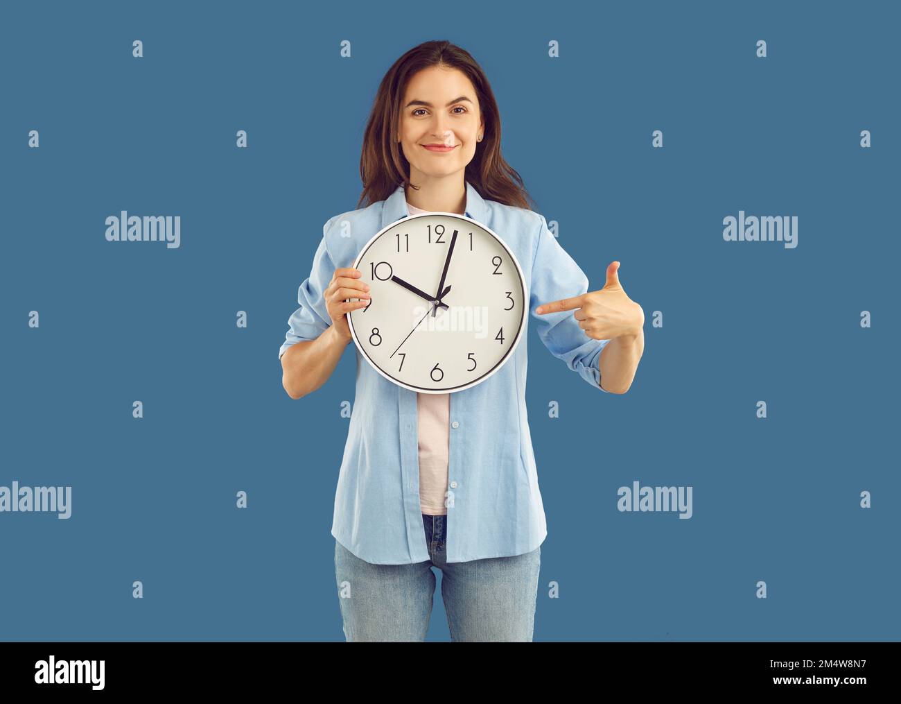 Portrait of beautiful happy young brunette holding round wall clock. Stock Photo