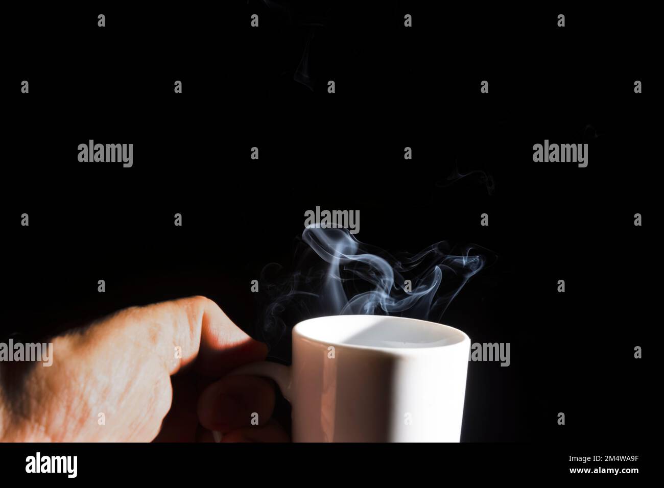 A closeup of a white cup against a black background with smoke coming out of it Stock Photo