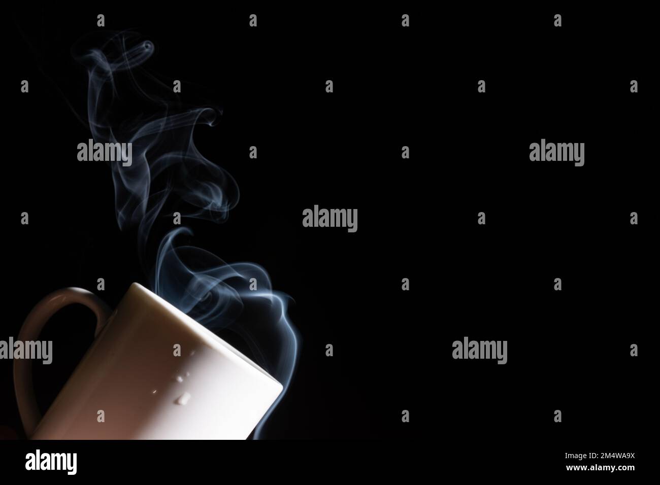 A closeup of a white cup against a black background with smoke coming out of it Stock Photo