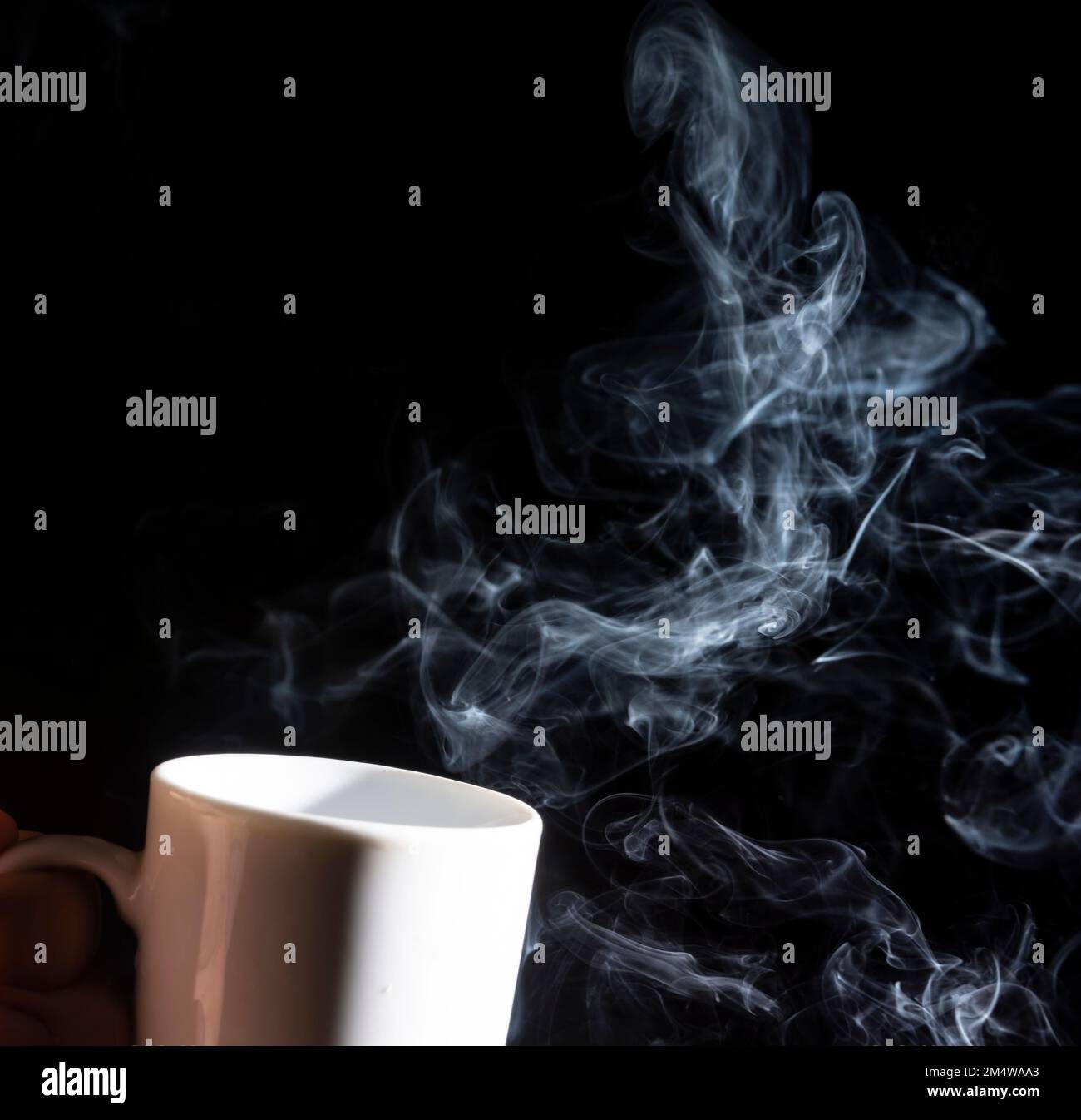 A closeup of a white cup against a black background with smoke coming out of it Stock Photo