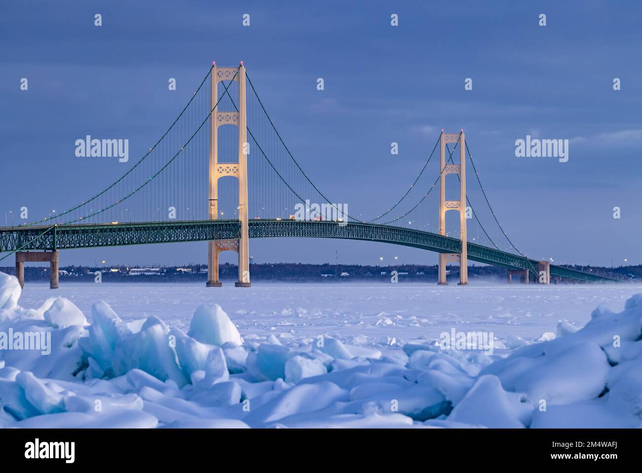 Mackinac Bridge in winter. Blue ice stacks on the shoreline in this frigid scene at the Straits of Mackinac. Stock Photo