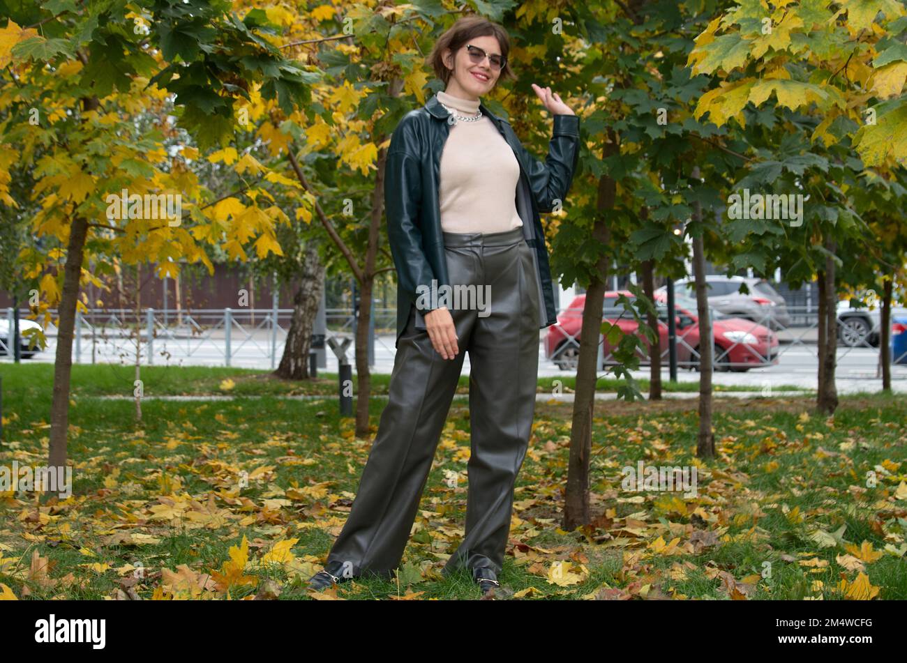 A woman in leather clothes stands against the backdrop of an autumn maple square Stock Photo