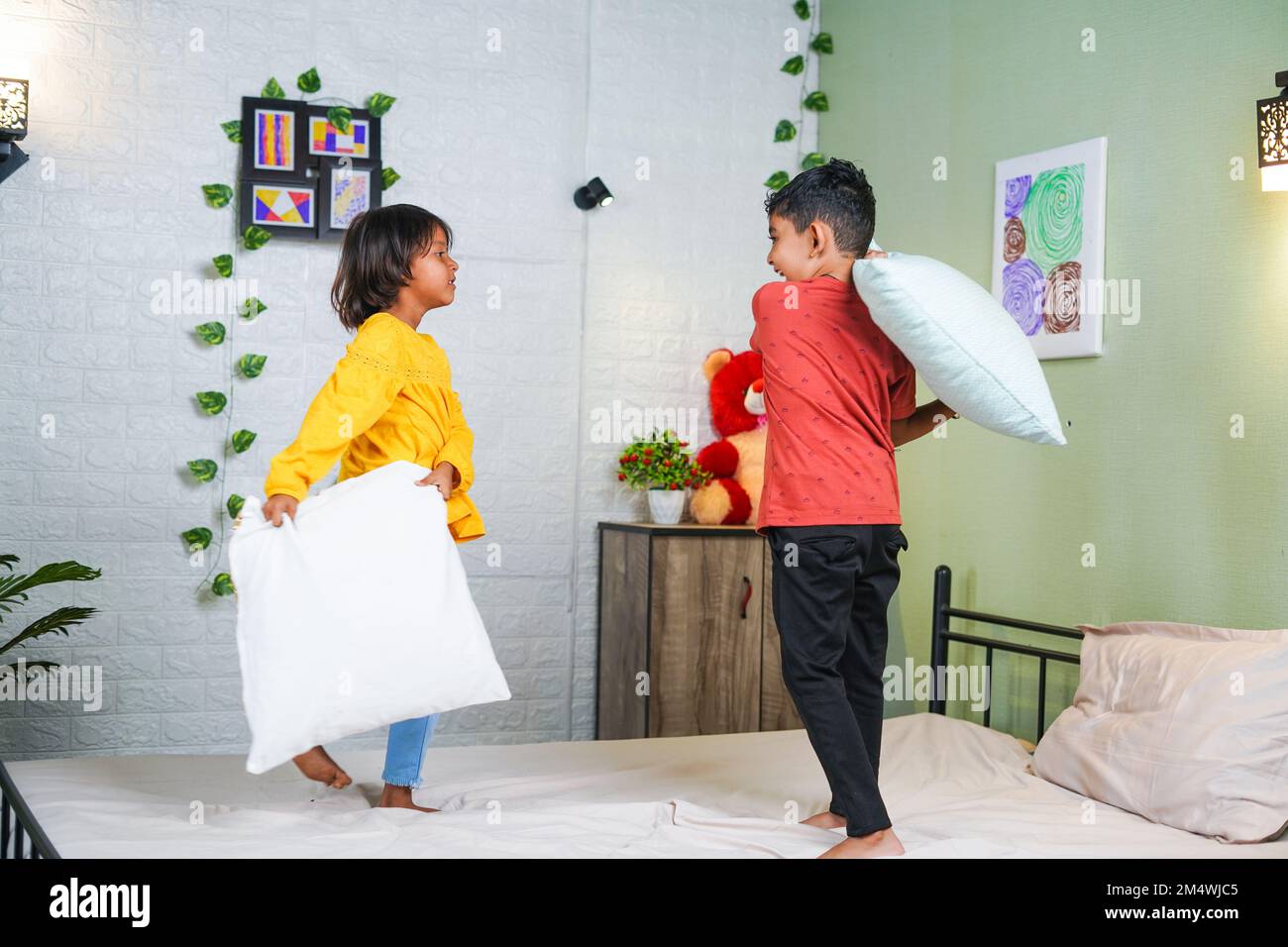 Young playful sibling kids fighting with pillow on bed at home - concept of relationship, childhood quarrel and bonding Stock Photo