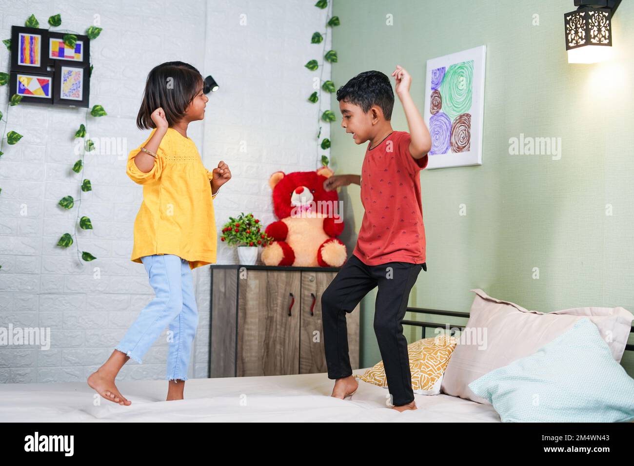 Happy smiling sibling kids dancing by jumping on bed at home - concept of playful childhood, bonding and relationship. Stock Photo