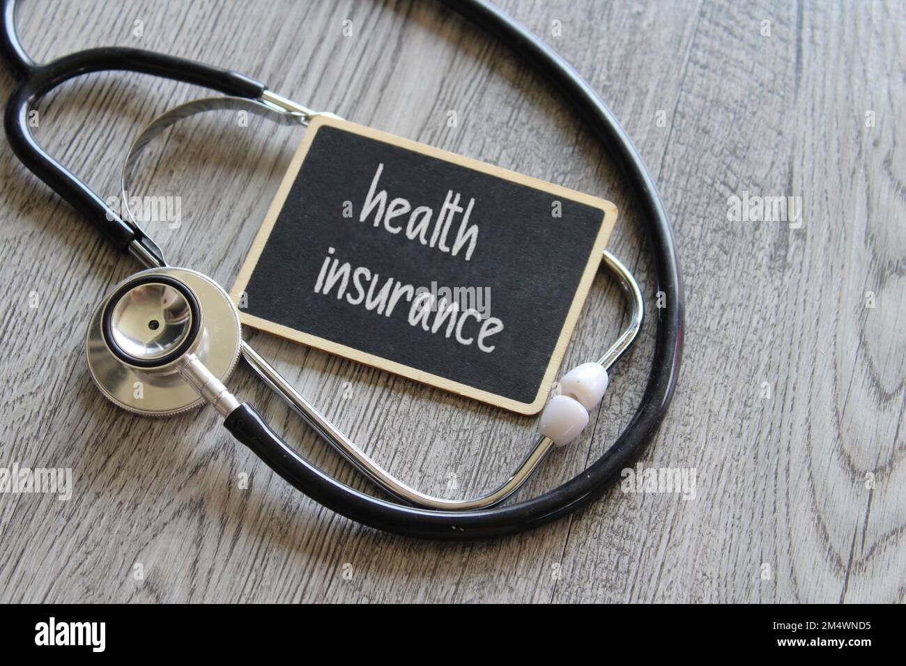Stethoscope and chalkboard with text HEALTH INSURANCE on wooden table. Medical and healthcare concept Stock Photo