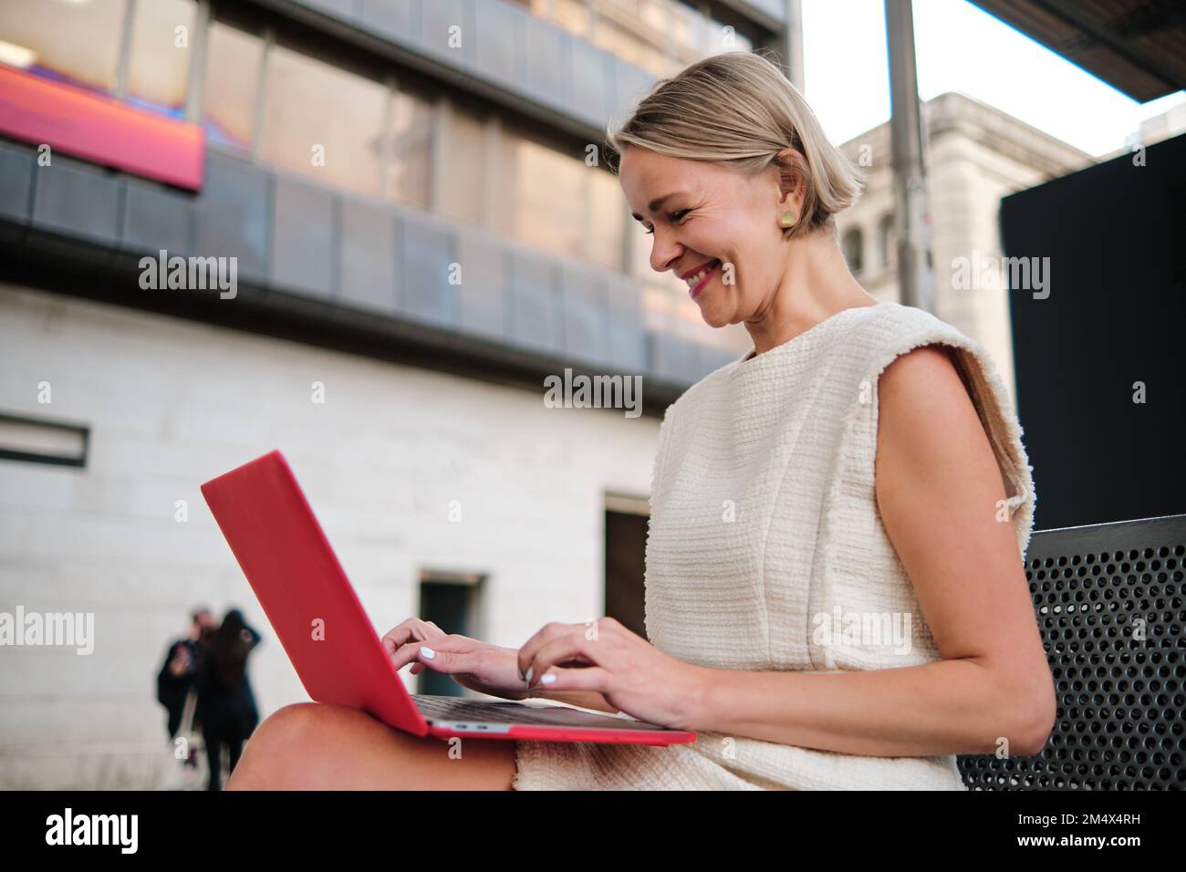 Businesswoman smiling while using a laptop sitting outdoors. Stock Photo