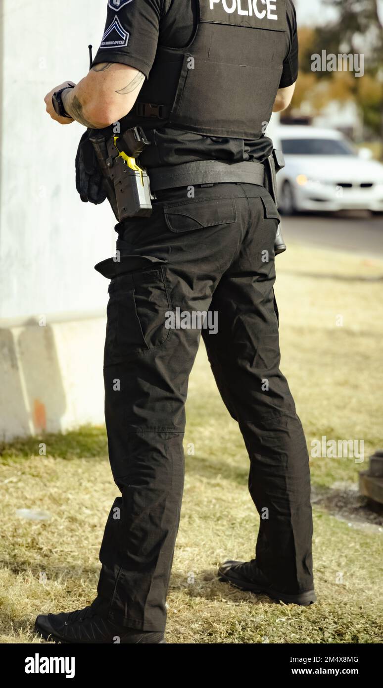 White male police officer cop standing on grass in a park during the day talking with person. Cop holding something in hand. Wearing bullet proof jack Stock Photo
