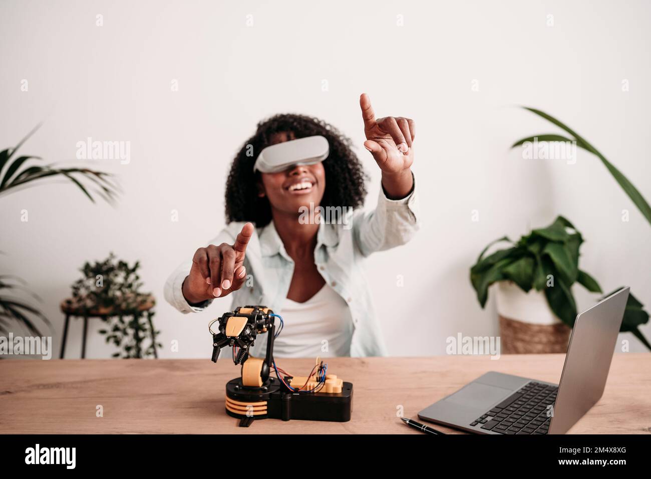 Smiling freelancer enjoying virtual reality headset with robotic model ...