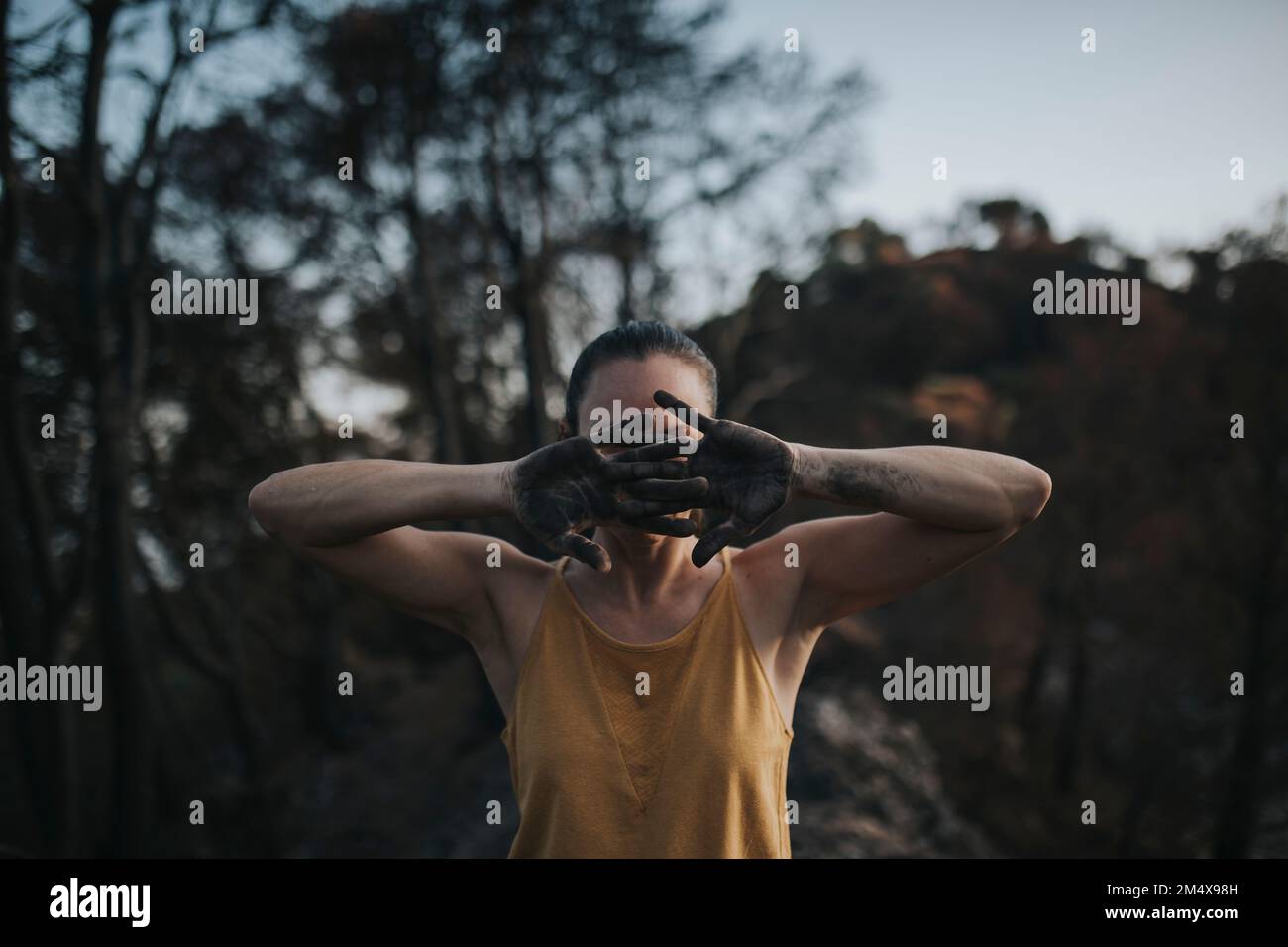 Woman hiding face behind hands black with ash in burnt forest Stock Photo