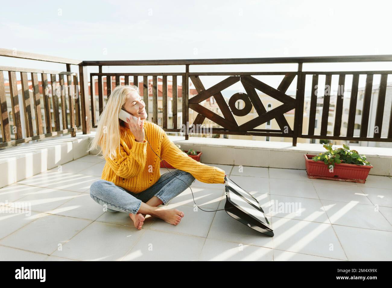 Woman talking over smart phone phone with charging solar panel on terrace Stock Photo