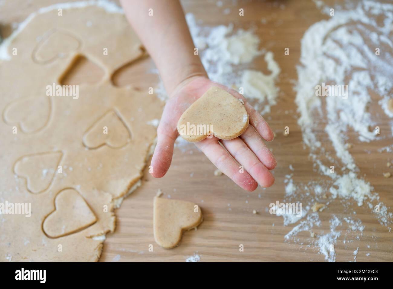 Hand of girl holding heart shaped cookie dough on table at home Stock Photo