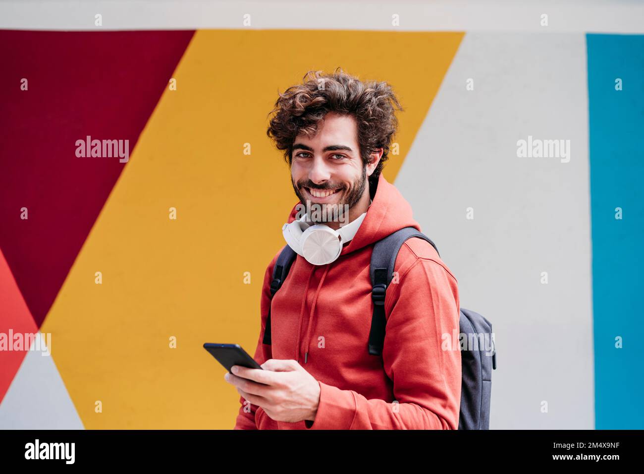 Smiling young man with smart phone in front of colorful wall Stock ...