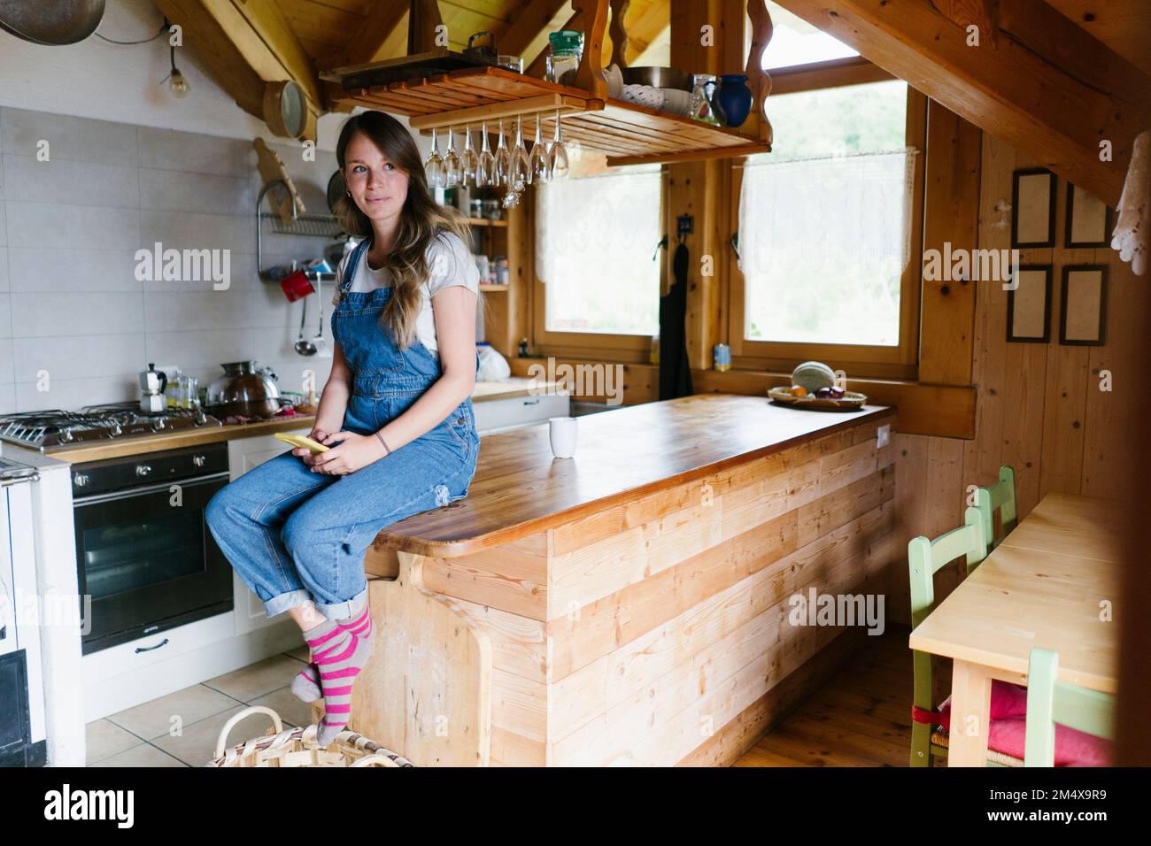 Thoughtful woman with smart phone sitting on kitchen island Stock Photo