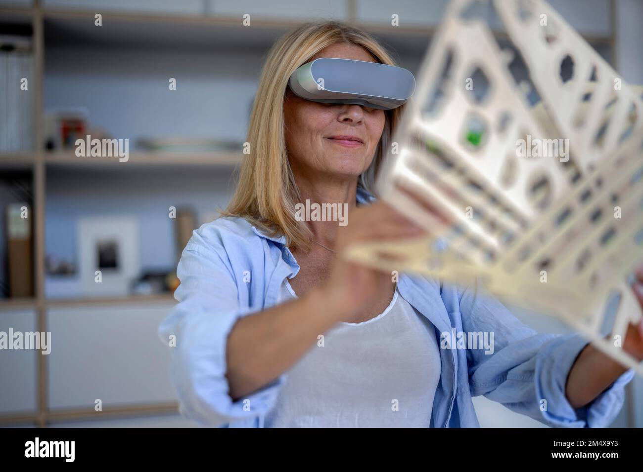 Smiling mature woman with VR glasses holding 3d print at home Stock Photo