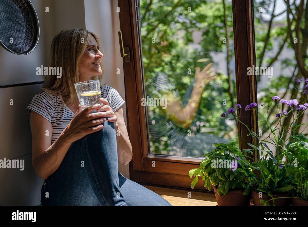 Mature woman day dreaming with glass of water near window Stock Photo