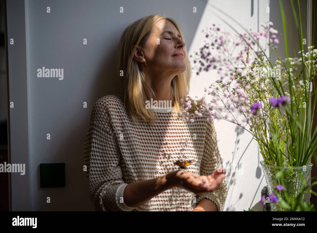 Mature woman standing with butterfly on hand at home Stock Photo